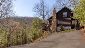 Eine Hütte mit Steinofen, einer Holzterrasse und einer Auffahrt zu einer Garage.