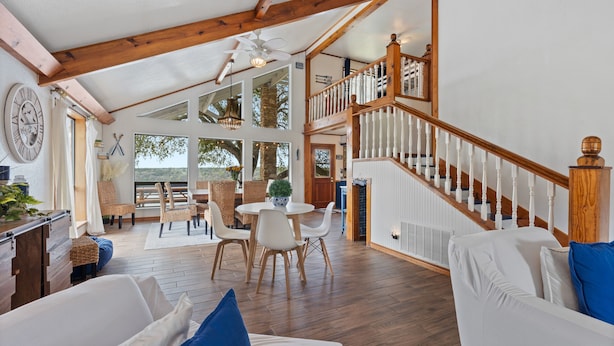 Een ruime woonkamer met een houten trap, een eettafel en een groot raam met uitzicht op de omgeving.