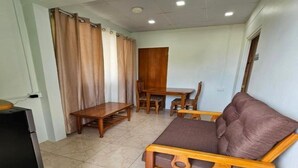 Um espaço de estar compacto com sofá, mesa de jantar e cadeiras. Uma pequena geladeira visível no canto.