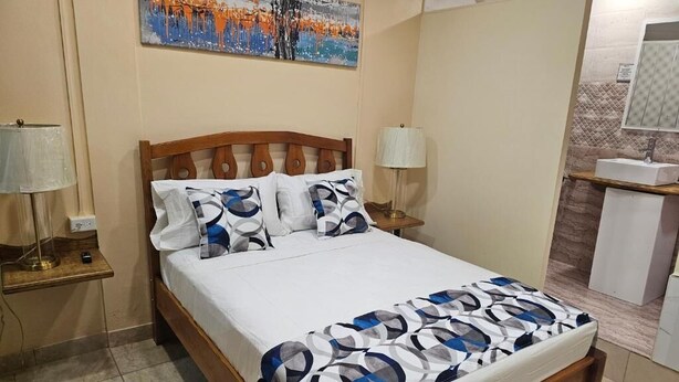 Quarto com cama de madeira, roupa de cama branca e um quadro na parede.