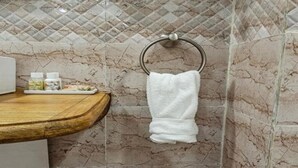 Casa de banho com painel de parede em mármore, bancada de madeira e porta-toalhas com toalha branca.