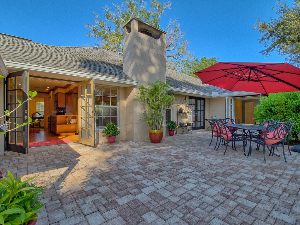 A patio with a brick floor, a red umbrella, and outdoor furniture.