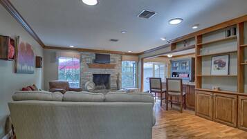 A spacious living room with a large sofa, a fireplace, wooden flooring, and built-in shelving.
