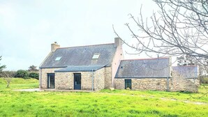 A stone house with a sloped roof and two skylights, surrounded by a grassy field. - Charming house 100 mt from the famous "La Torche" beach

 (Plomeur)