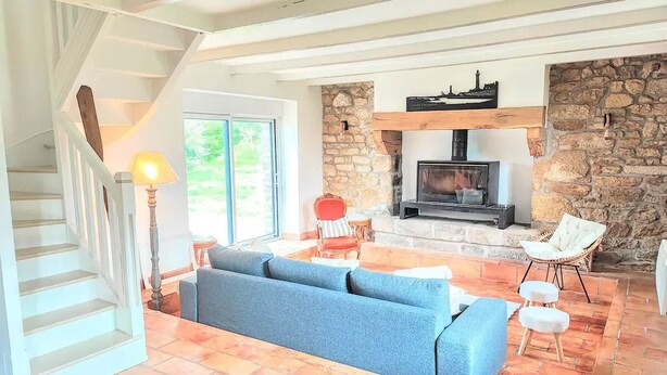 A spacious living area with a stone fireplace, a blue sofa, and a staircase leading to an upper level. - Charming house 100 mt from the famous "La Torche" beach

 (Plomeur)