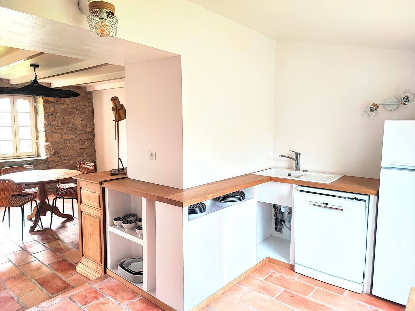 Una cocina compacta con zona de comedor, pared de piedra y ventana.