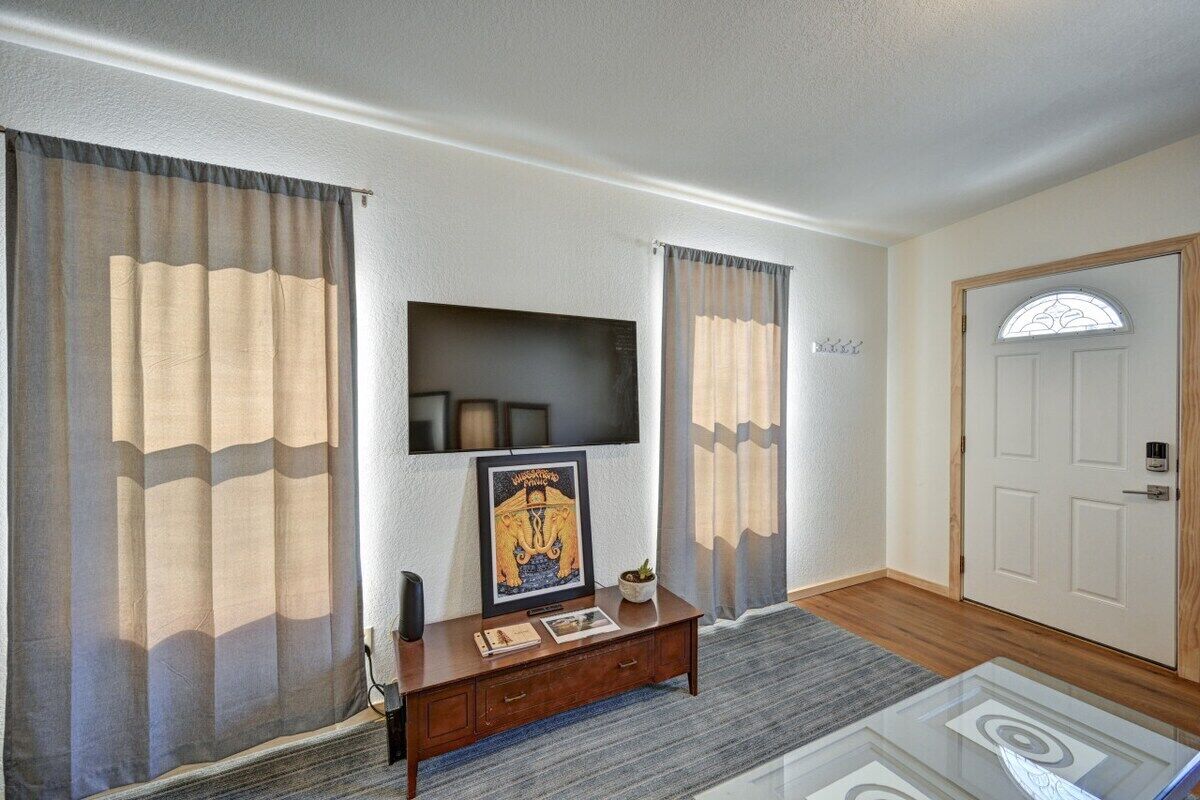 A room with a flat-screen TV mounted on the wall, a wooden console table with a framed picture, and a door with a window.