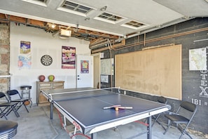 Una mesa de ping pong en una habitación con dardos, carteles y un mapa en la pared.