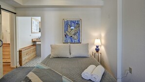 Une chambre d’hôtel avec un lit, une table de chevet avec une lampe, un tableau représentant un oiseau accroché au mur et une vue sur la salle de bain.