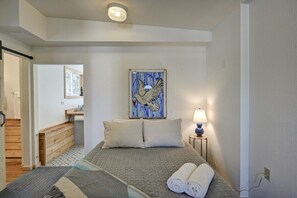 A hotel room with a bed, a nightstand with a lamp, a painting of a bird on the wall, and a view of a bathroom.