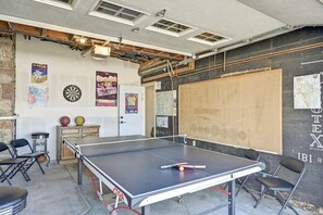 A ping pong table in a room with a dartboard, chairs, and posters on the wall.