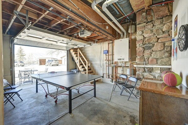Amplio espacio interior con mesa de ping pong, sillas, una pared de piedra y una escalera que lleva a un nivel superior.