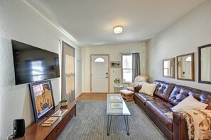 A living room with a brown leather sofa, a flat-screen TV mounted on the wall, and a framed picture on the wall.