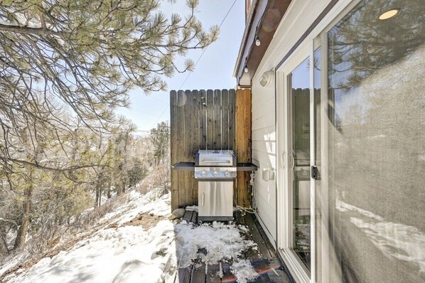 A wooden deck with a barbecue grill, a sliding glass door, and a snowy landscape.
