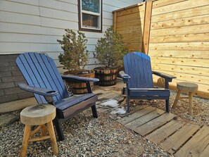 Dos sillas Adirondack con patas de madera y estructura metálica, ubicadas en una terraza de madera con suelo de grava.