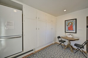 A compact kitchen with a refrigerator, white cabinets, a dining table with chairs, and a patterned floor.