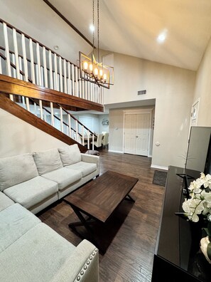 A modern living room with a sectional sofa, a coffee table, a TV stand, and a staircase with a railing.