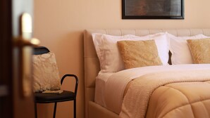Ein Schlafzimmer mit einem Bett, Kissen, einem Sessel, einem Teppich und einem gerahmten Bild an der Wand.
