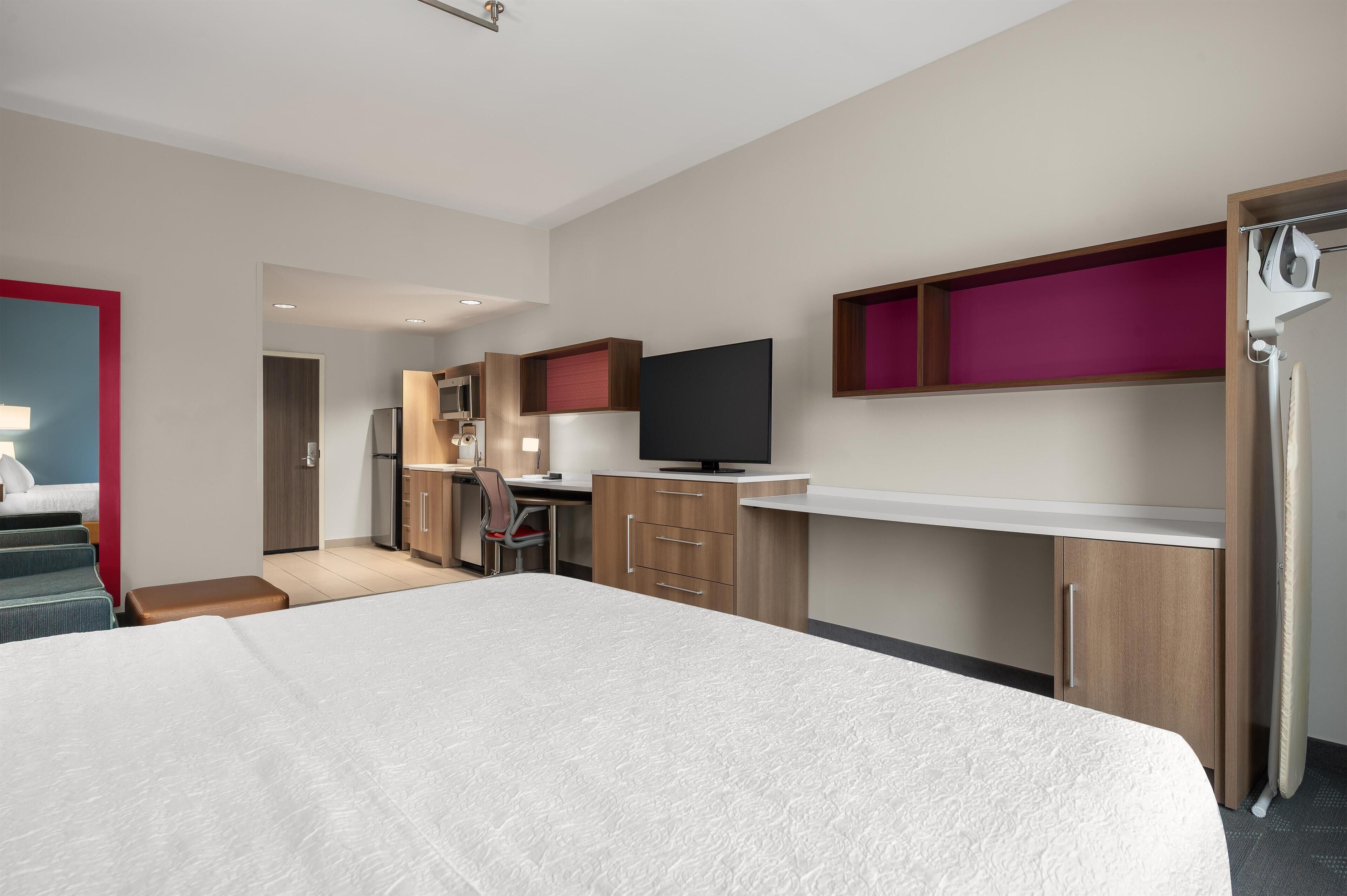 Una habitación de hotel moderna con una cama grande, kitchenette, televisor y baño.