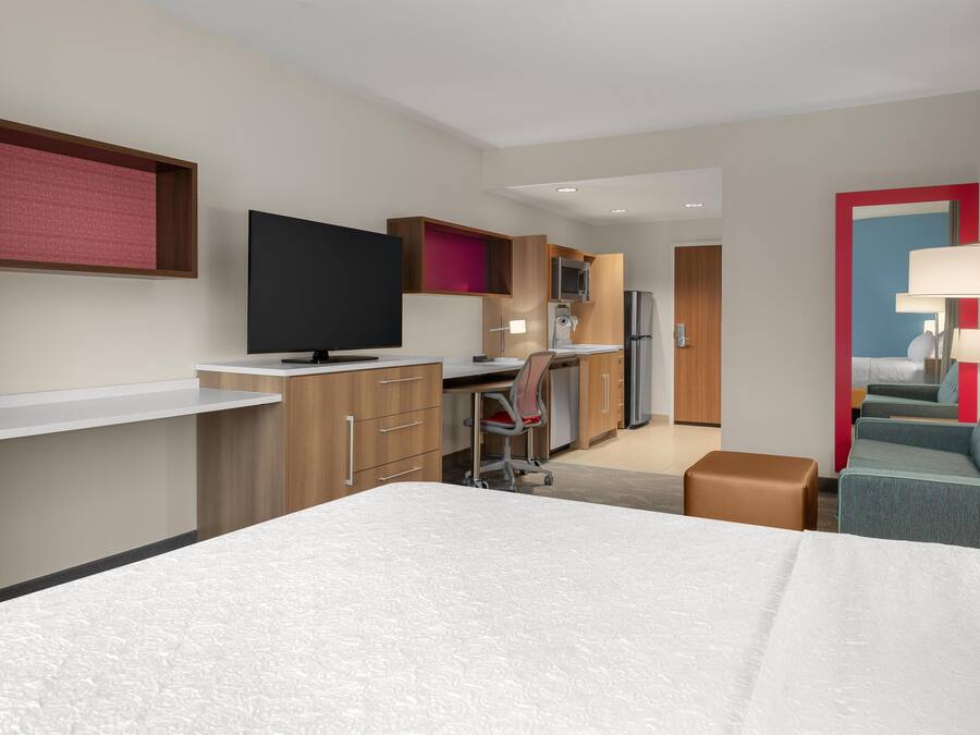 Ein Hotelzimmer mit Bett, Schreibtisch mit Computer, Küchenzeile und einer Sitzecke mit Sofa und Sesseln.