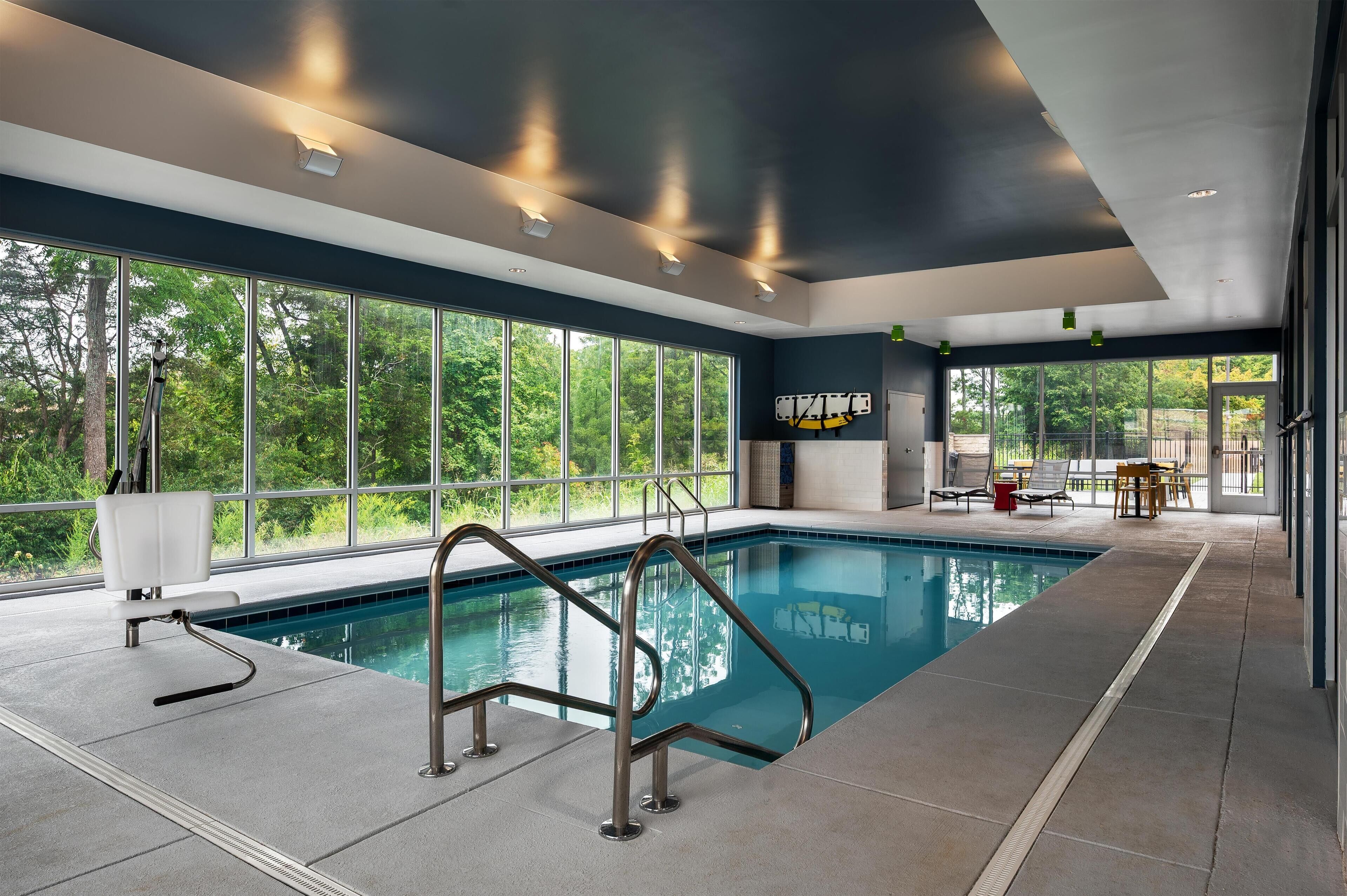 Una piscina interior con paredes de vidrio transparente, un diseño moderno de techo y vistas a zonas verdes exteriores.