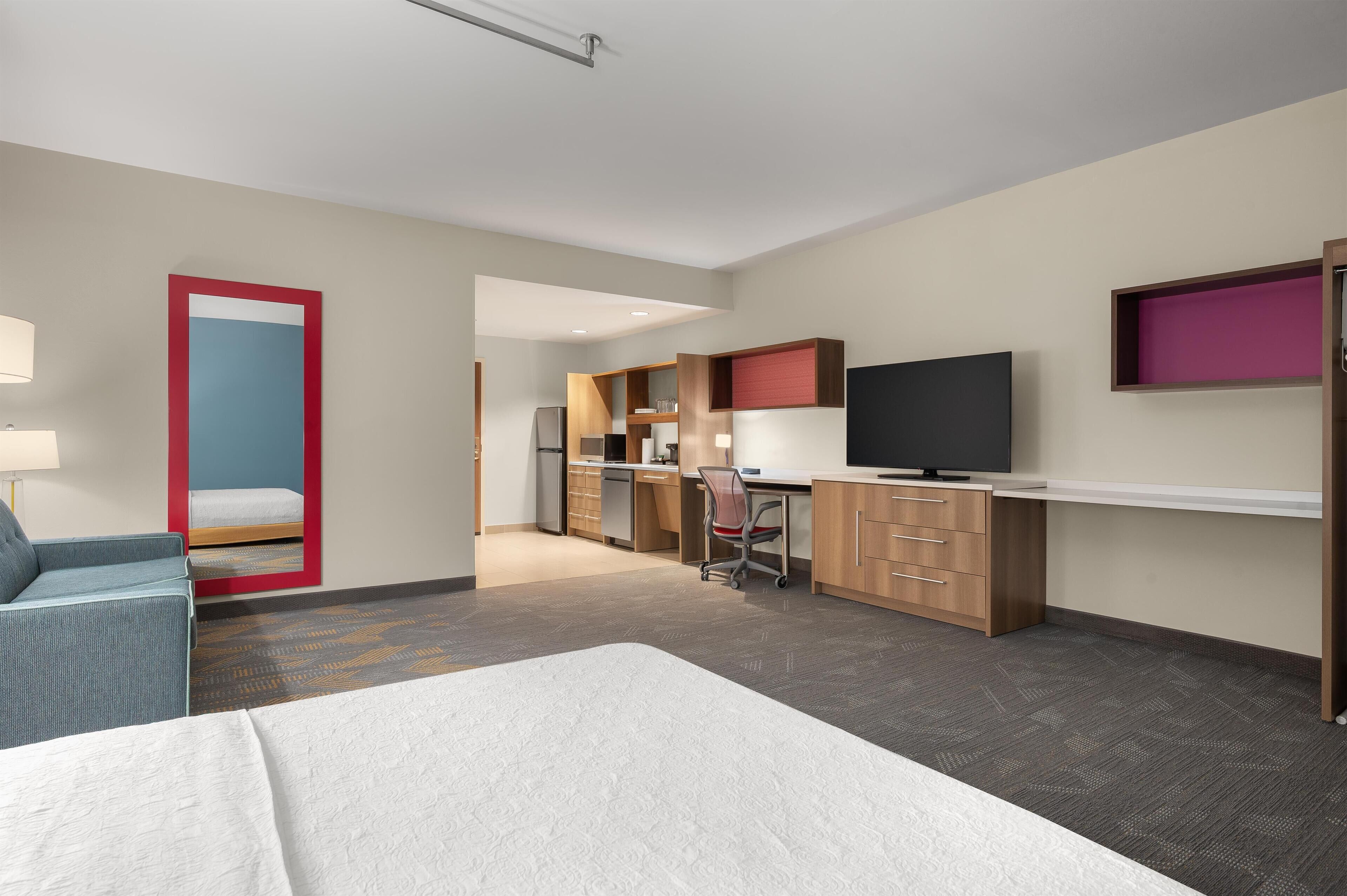 Una habitación de hotel moderna con cama, escritorio, silla, televisor y kitchenette.