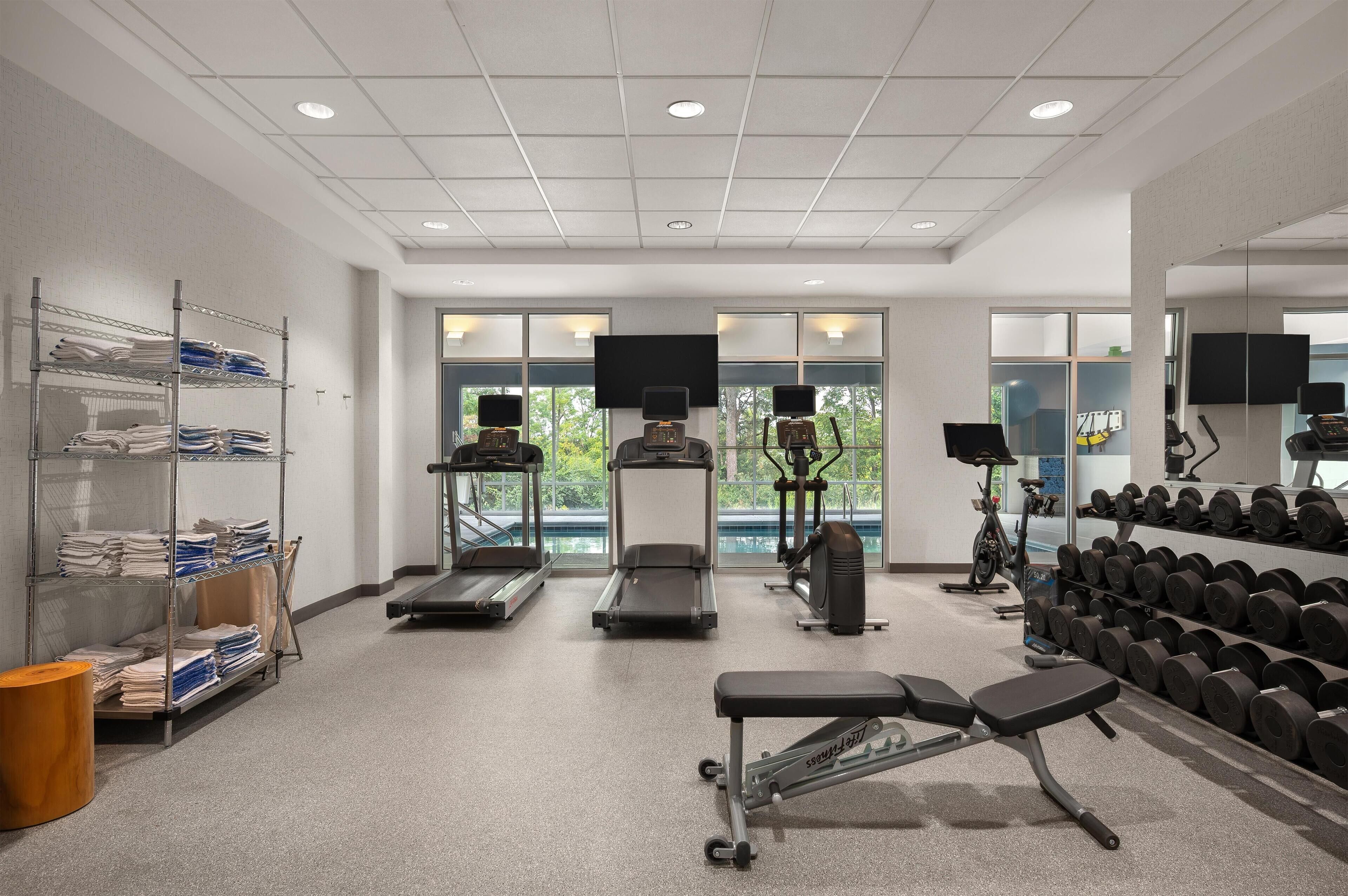 A modern gym with treadmills, elliptical machines, a bench, and a rack of dumbbells.