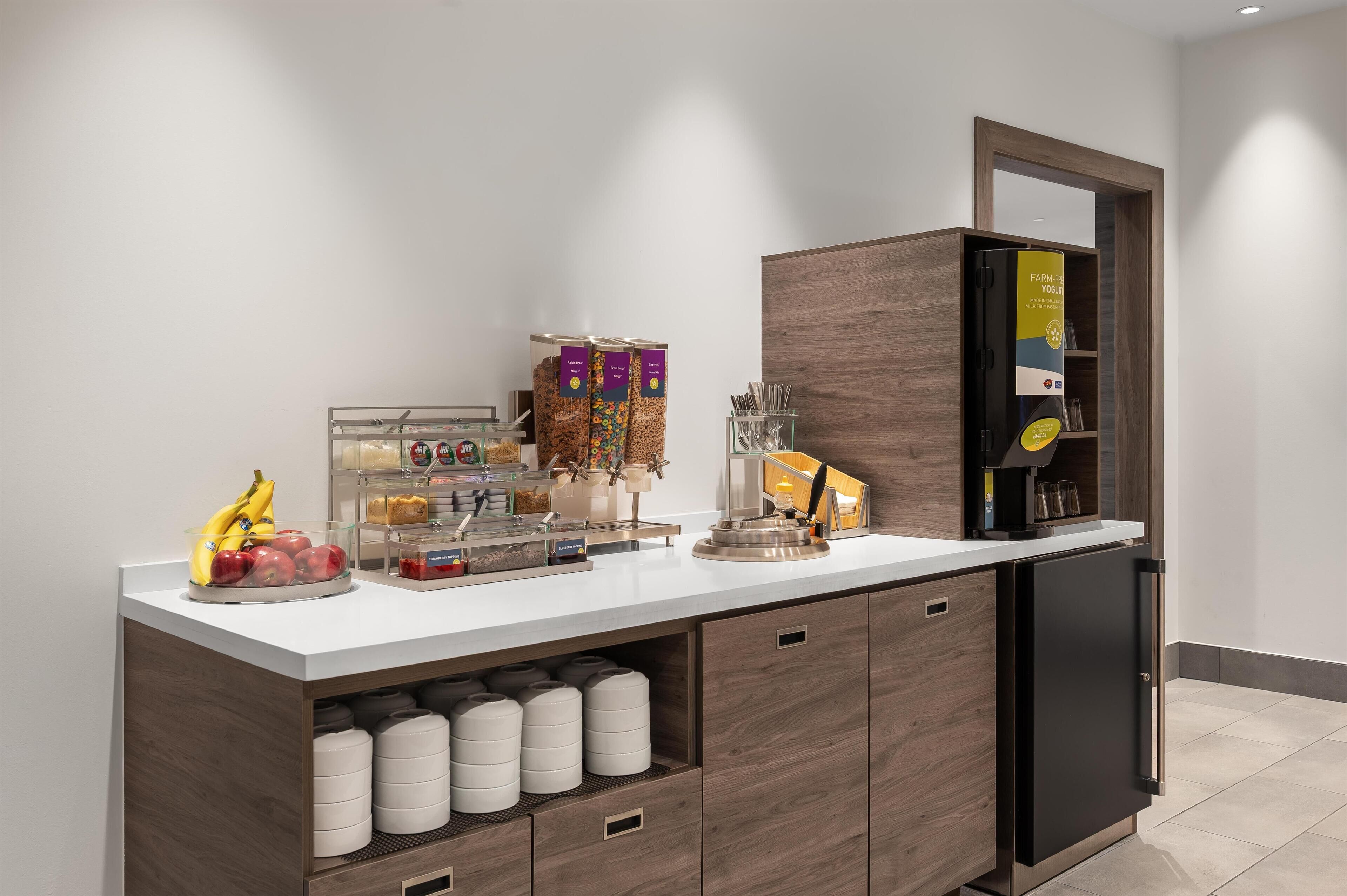 Un área de cocina moderna con un refrigerador empotrado, una cafetera y varios alimentos sobre la encimera.