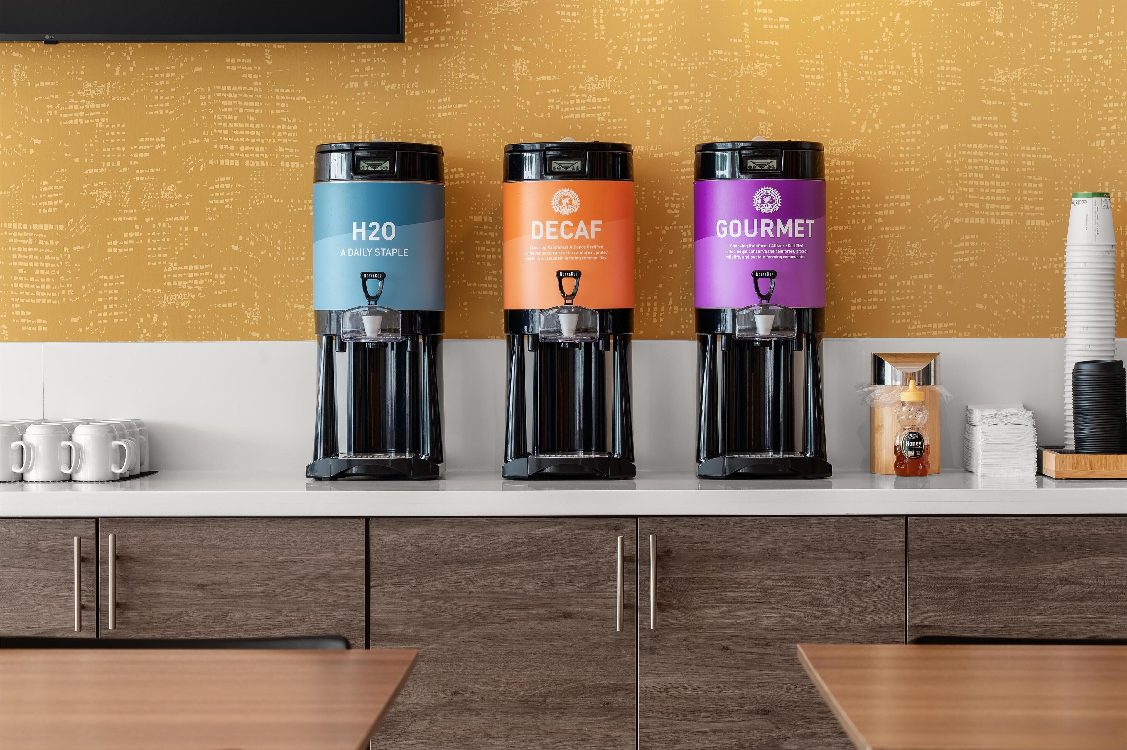 Drie koffieautomaten met de aanduiding H2O, Decaf en Gourmet op een aanrecht.