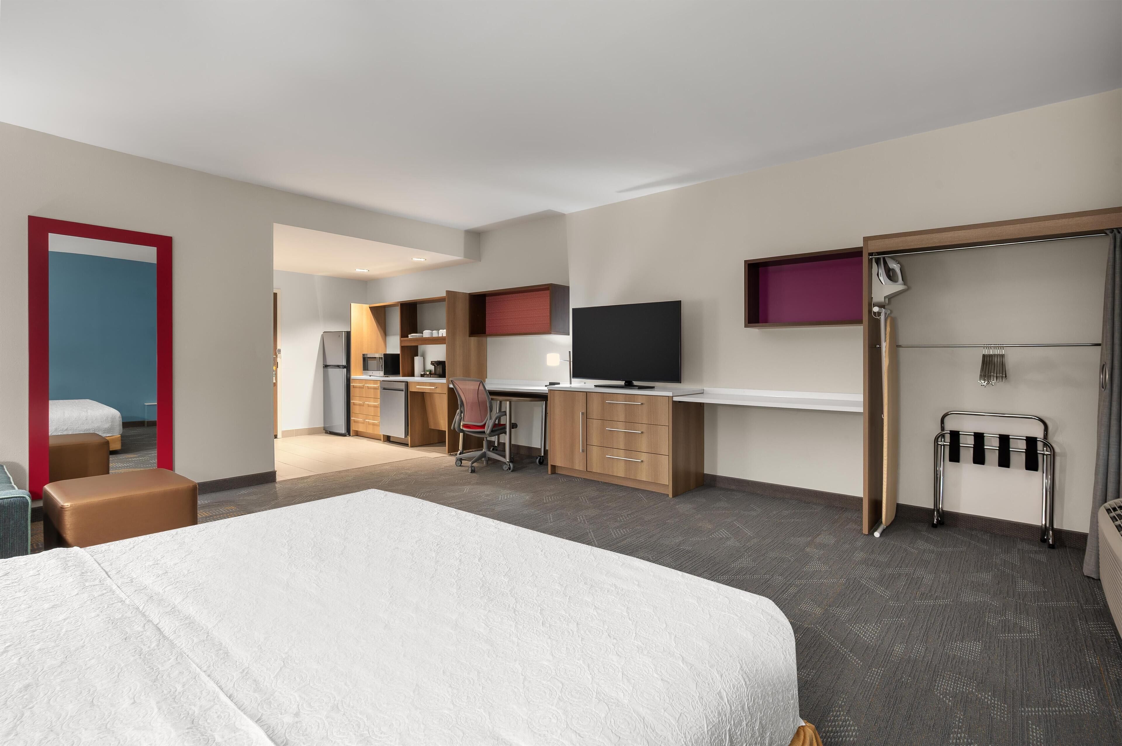 A hotel room with a bed, a desk, a chair, a television, a wardrobe, and a shower area.