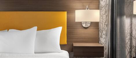 A hotel room with a wooden headboard, a bedside table with a lamp, and a patterned wallpaper.