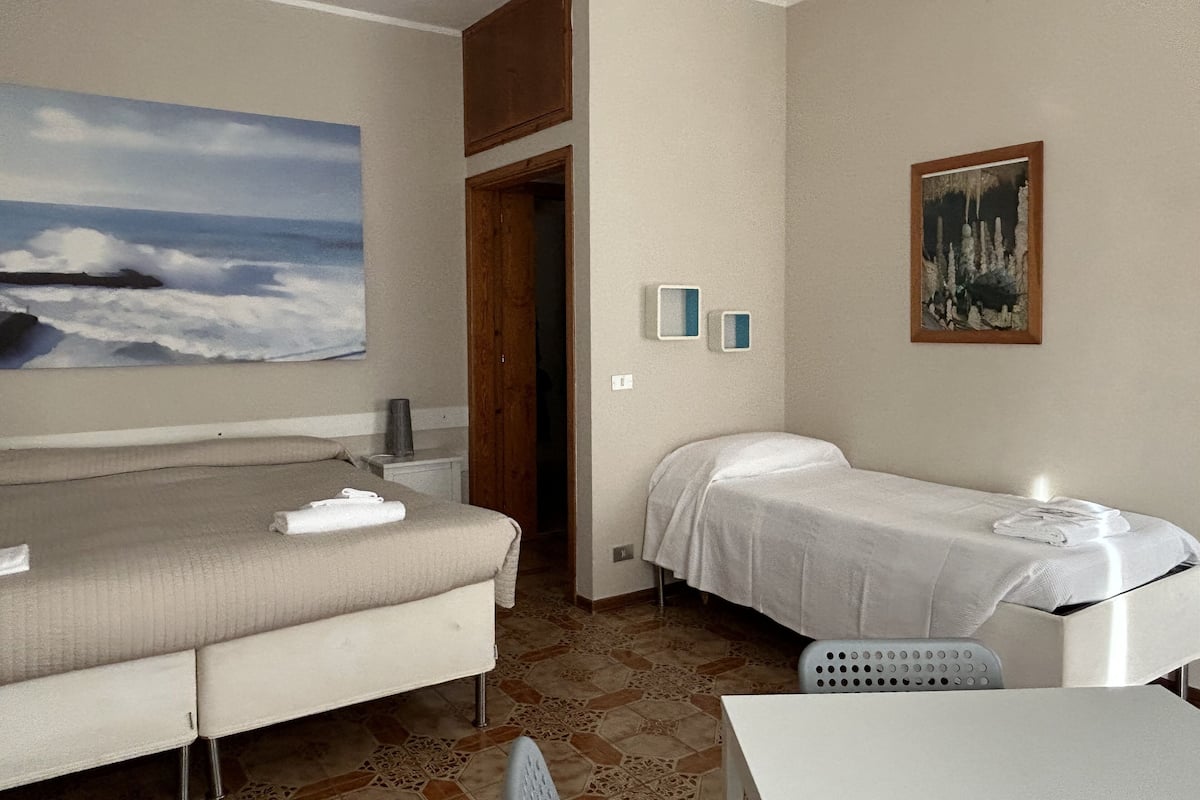 A room with a bed, a small table, and a painting of a beach scene.