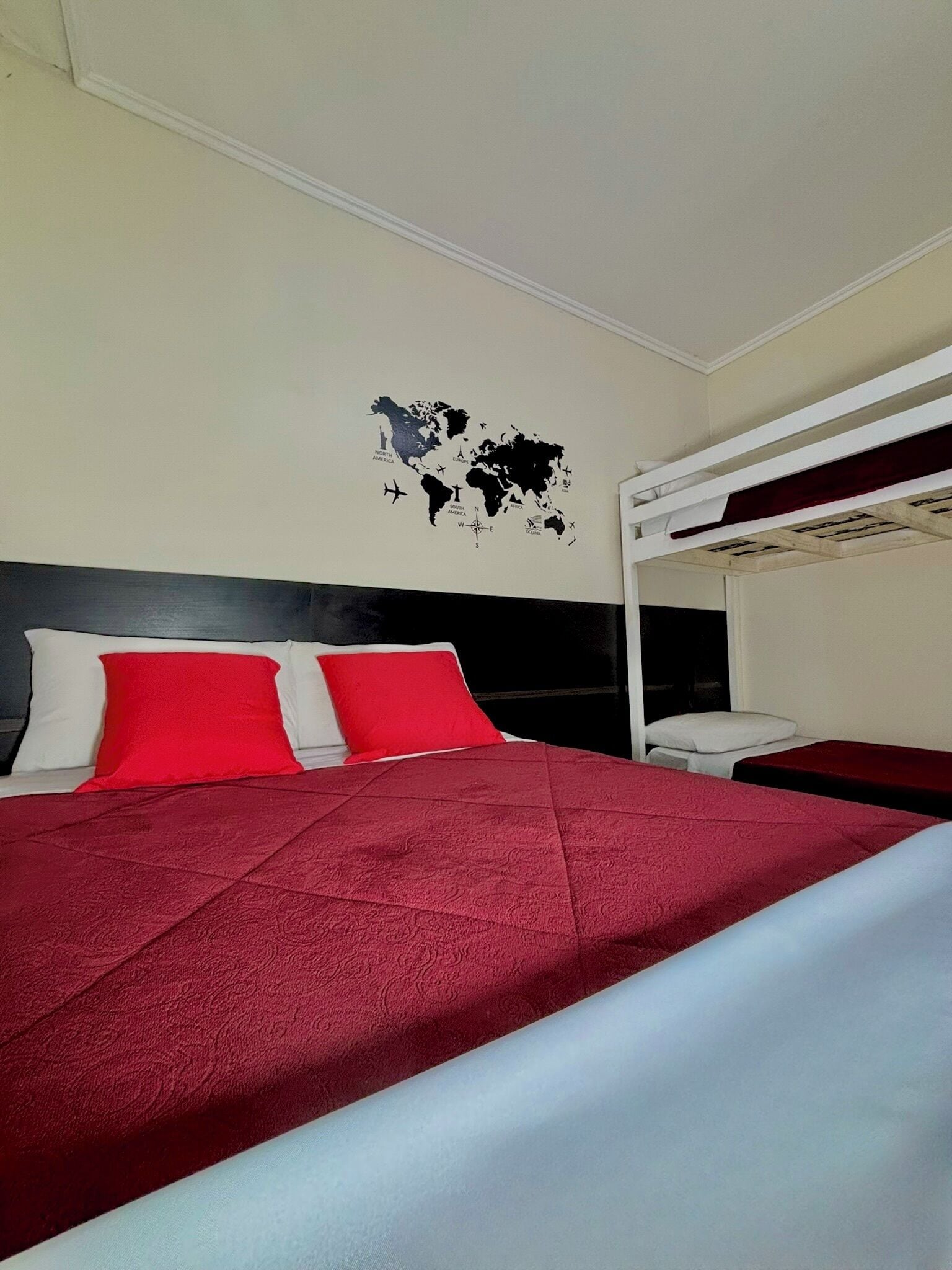 Une chambre d’hôtel avec un lit, des oreillers rouges et blancs, une carte du monde accrochée au mur et un lit superposé.
