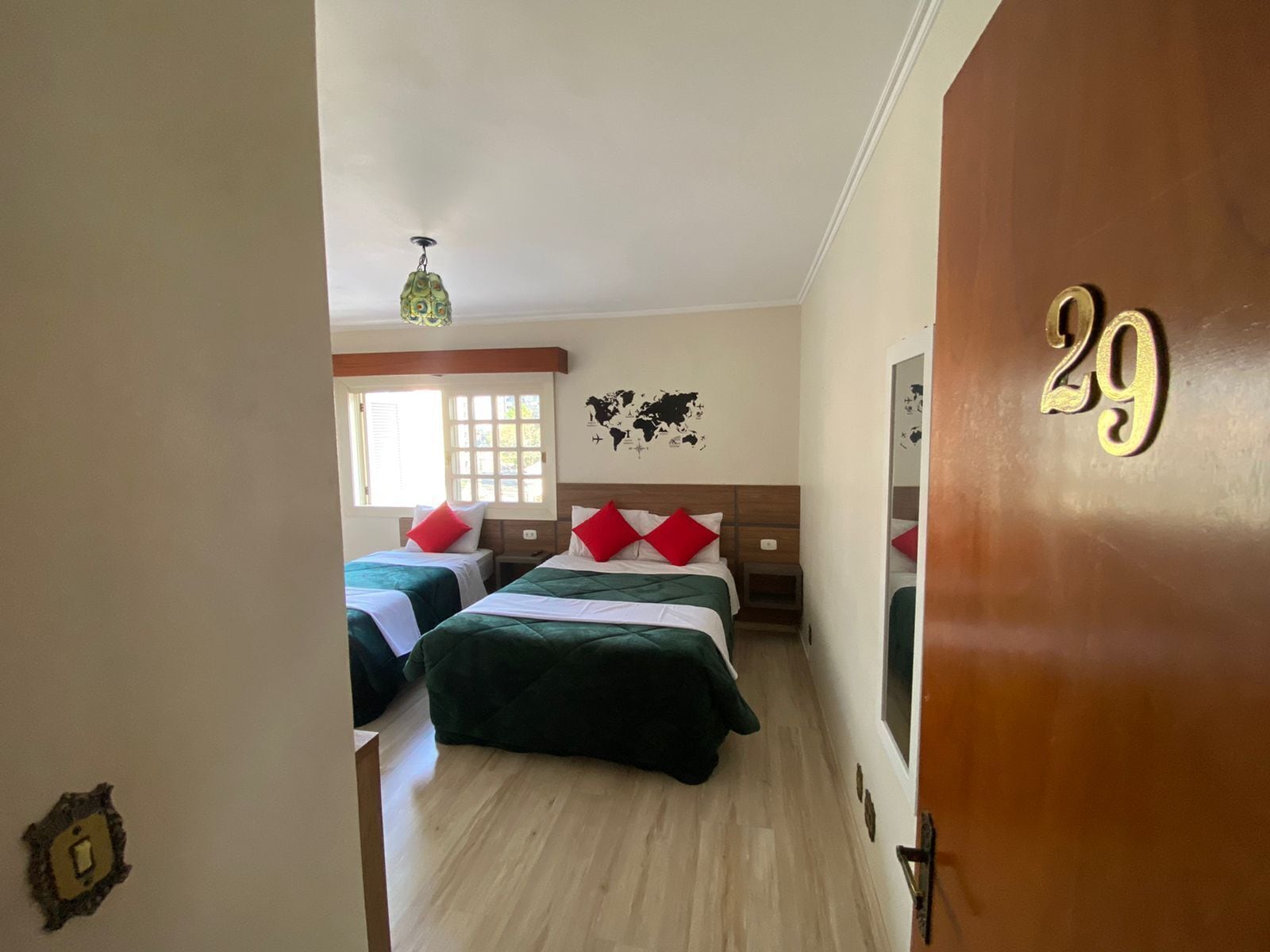 A hotel room with two beds, a wooden door with the number 29, a world map on the wall, and a ceiling fan.
