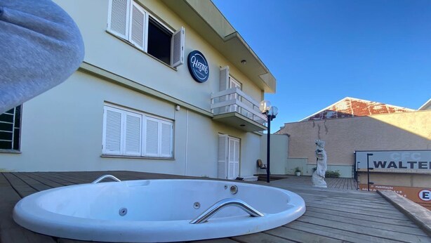 Uma banheira de hidromassagem em um deck de madeira, um edifício com varanda e uma estátua ao fundo.