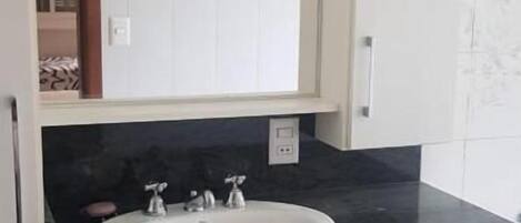 Un baño con lavamanos blanco, encimera negra y armarios blancos.