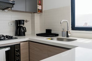 A modern kitchen with a coffee maker, a sink, and a window with a city view. - Apartamento Exclusivo en Laureles (Medellín)