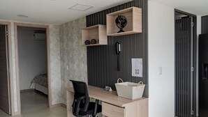 Ett modernt sovrum med ett skrivbord i trä, en svart kontorsstol, en jordglob på en hylla, ett sängbord och en säng med ett mönstrat överkast.