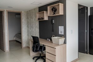 A modern bedroom with a wooden desk, a black office chair, a globe on a shelf, a bedside table, and a bed with a patterned bedspread. - Apartamento Exclusivo en Laureles (Medellín)