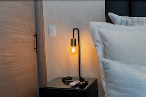 A bedside table with a lamp, a remote control, and a power outlet. - Apartamento Exclusivo en Laureles (Medellín)