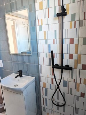 Ein Badezimmer mit einem weißen Waschbecken, einem Spiegel und einer Dusche mit farbenfroher Fliesenrückwand.