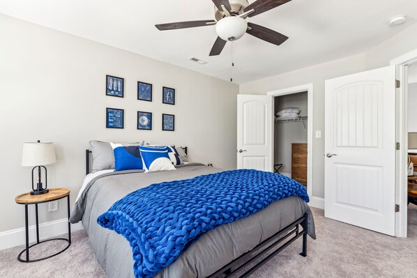 A bedroom with a bed, a ceiling fan, a nightstand, a lamp, and a wardrobe. - Pinehurst Grand Slam (West End)