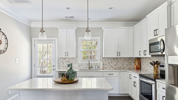 A modern kitchen with white cabinets, stainless steel appliances, and a central island with stools. - Pinehurst Grand Slam (West End)