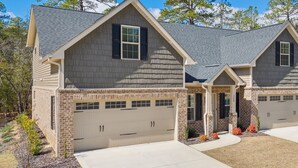 A two-story house with a garage, brick foundation, and a sloped roof. - Pinehurst Grand Slam (West End)