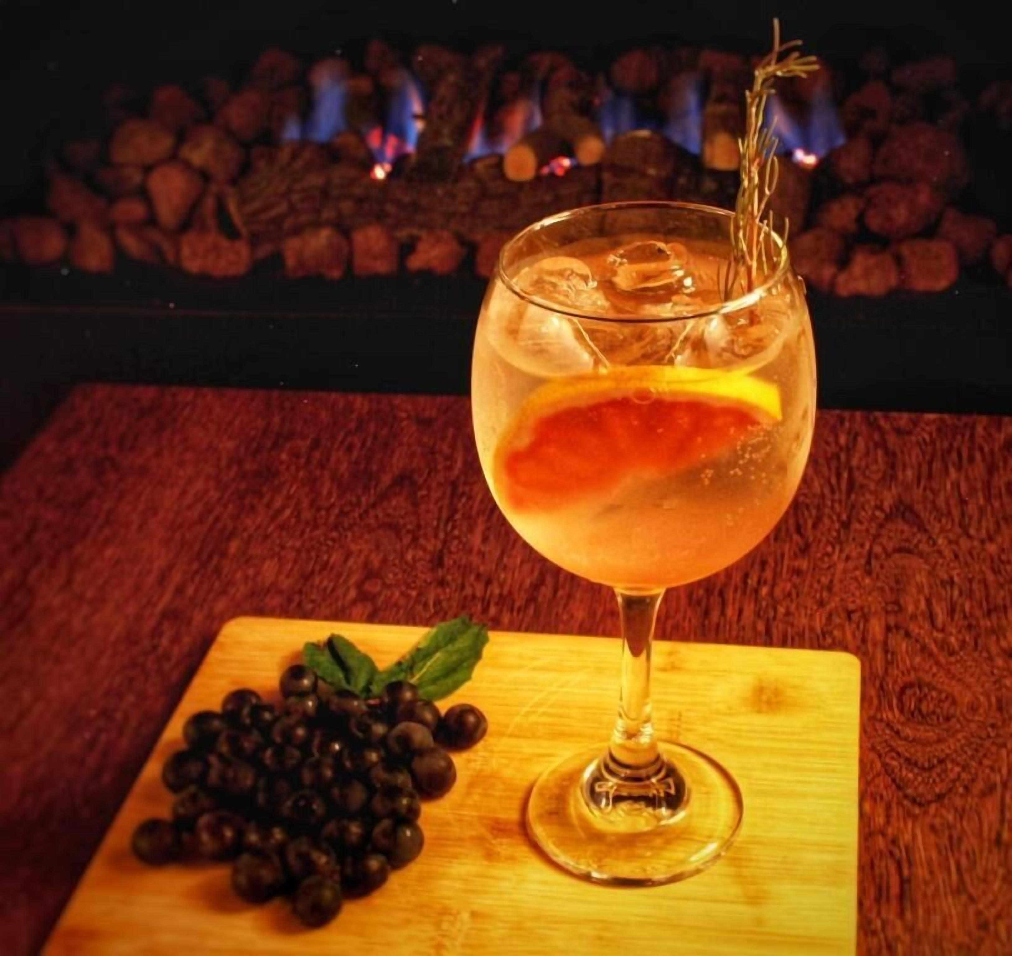 Una copa de cóctel con una guarnición sobre un posavasos de madera, junto con un racimo de uvas negras.