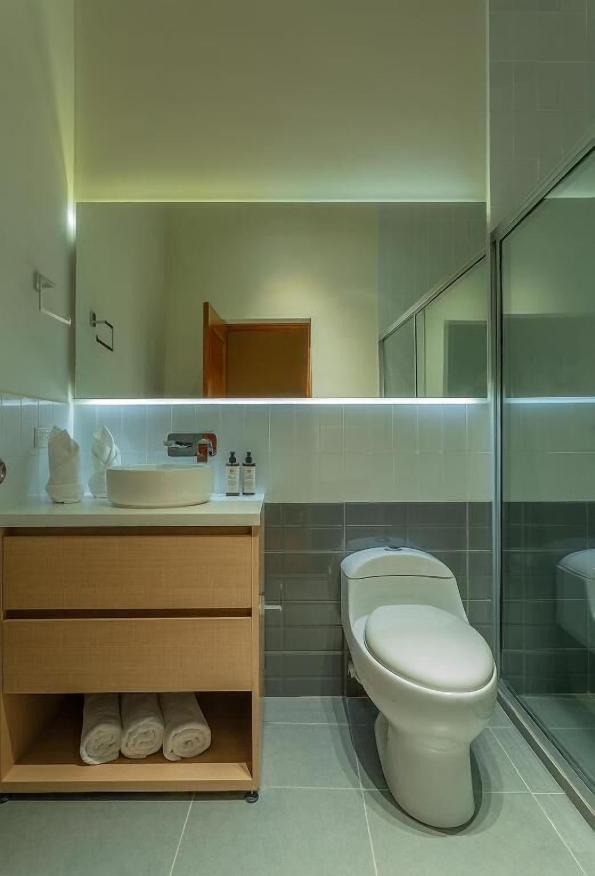 A modern bathroom with a white sink, mirror, and toilet. There are towels and toiletries on the sink.