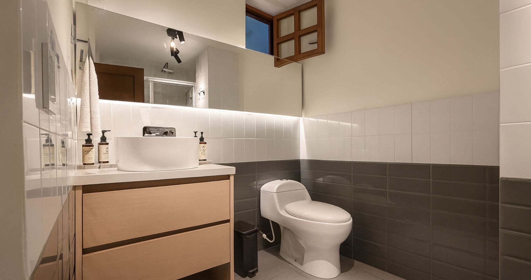 A modern bathroom with a white sink, mirror, and toilet.