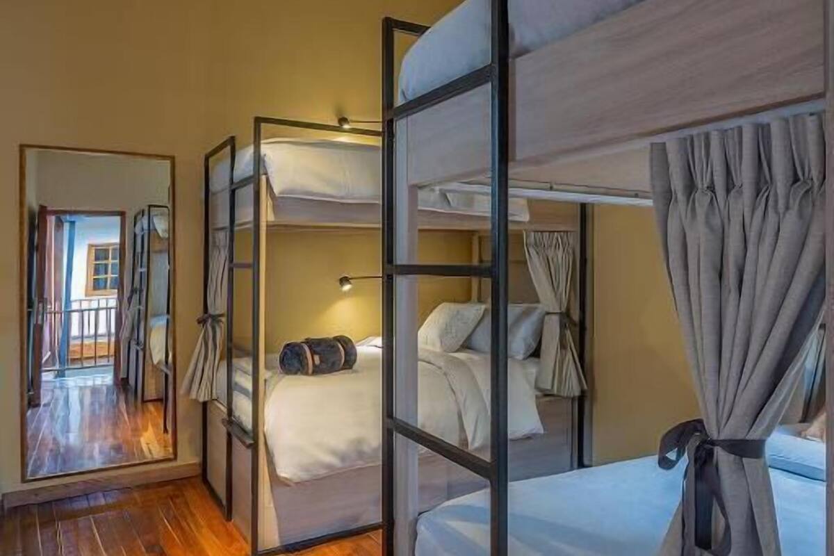 Een kamer met stapelbedden, houten vloeren, een spiegel en uitzicht op een buitenruimte.