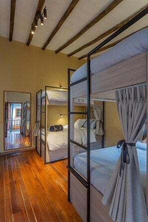 Ein Zimmer mit Etagenbetten, Holzboden, einem Spiegel und Blick auf einen Außenbereich.