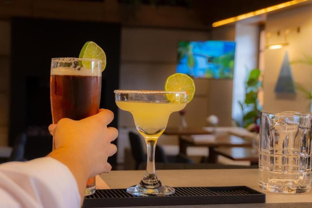 Duas bebidas sobre uma mesa, com uma televisão ao fundo.